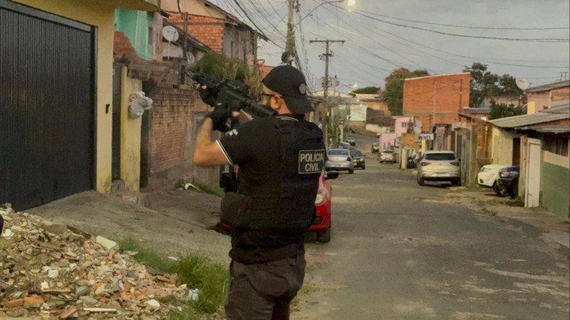 Policial civil é visto na rua empunhando fuzil para a casa do alvo.