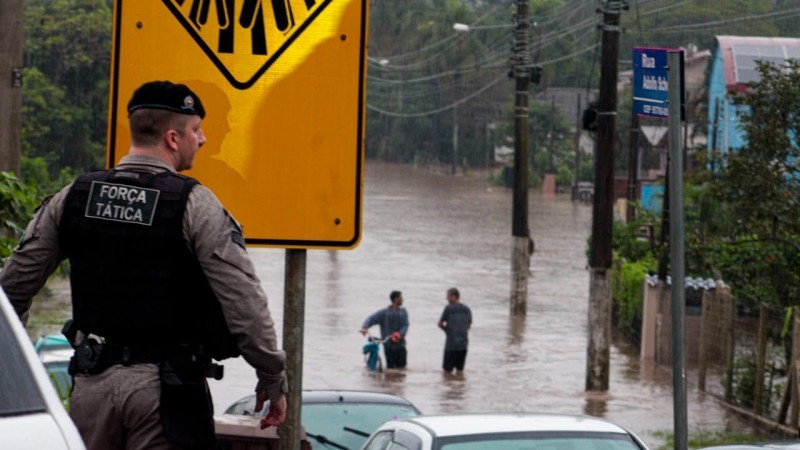 Imagem mostra policial militar da BM em frente a uma área inundada