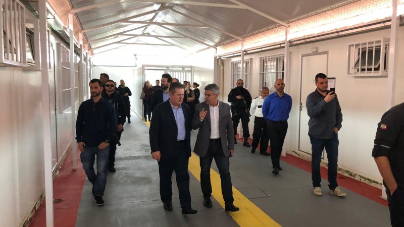 Ao centro da imagem, vice-governador e secretário da Administração Penitenciária, acompanhados de comitiva, caminham por corredor de presídio em Itajaí, Santa Catarina.