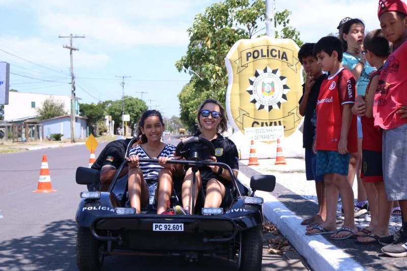 Policial Civil mulher e criança em mini buggy da instituição. Ao fundo, balão inflável do brasão da Polícia Civil.