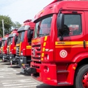 Saindo do lado direito da fotografia em primeiro plano um caminhão-tanque entregue ao Corpo de Bombeiros Militar do Rio Grande do Sul, estão dispostos mais outro quatro caminhões, um do lado do outro.