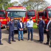 O governador Eduardo Leite, o vice-governador e secretário da Segurança Pública Ranolfo Vieira Júnior, o comandante-geral do CBMRS, coronel César Eduardo Bonfanti e três bombeiros estão dispostos um do lado do outro, de máscaras em frente aos caminhões