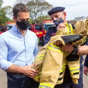 Em primeiro plano o governador Eduardo Leite está ao lado do comandante-geral do CBMRS, coronel César Eduardo Bonfanti, que está segurando um uniforme que será usado pelos bombeiros.