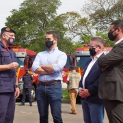 O coronel César Eduardo Bonfanti, o governador Eduardo Leite e o vice-governador e secretário da Segurança Pública Ranolfo Vieira Júnior estão um do lado do outro conversando e ao fundo há os caminhões-tanque