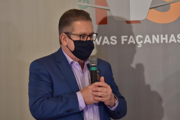 Vice-governador Ranolfo Vieira Júnior, de terno e máscara contra a Covid-19, segura um microfone com as duas mãos. Ao fundo, painel cinza com logo do governo do RS.