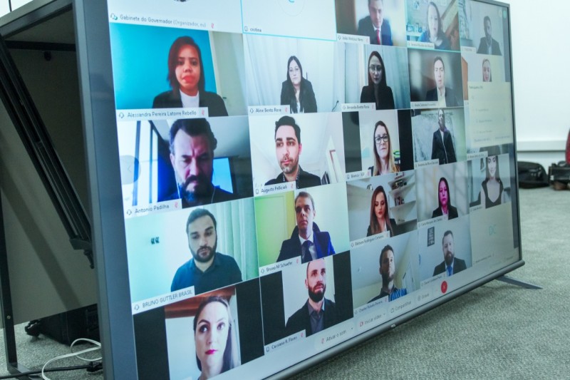 A imagem mostra um telão dividido em várias imagens dos formandos e familiares que acompanhavam a formatura por videoconferência