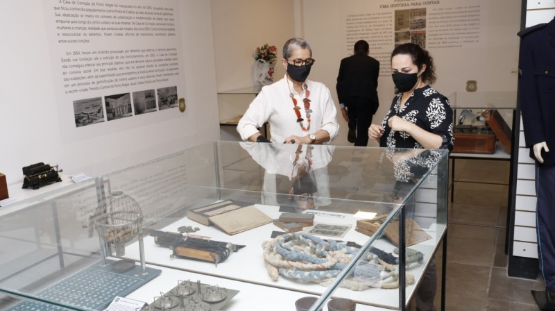 Uma redoma de vidro protege diversos objetos históricos que são observados por duas mulheres
