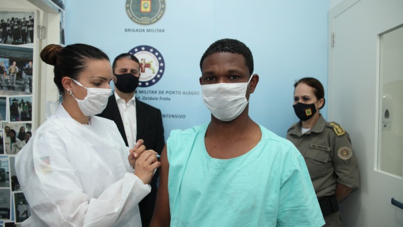 Enfermeira do Hospital da Brigada de Porto Alegre, vacinando o primeiro brigadiano, atrás deles, uma agente da BM e o Secretário da Segurança Pública Adjunto, Coronel Marcelo Gomes Frota.