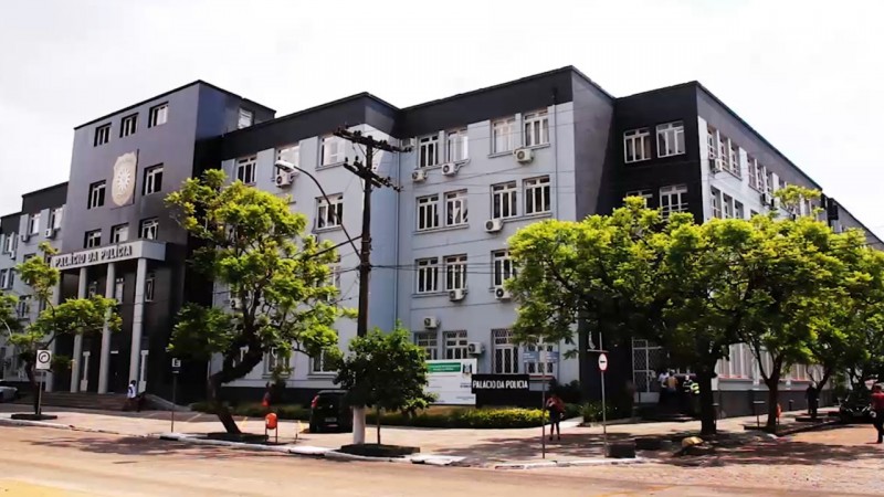 Parte externa do Palácio da Polícia de Porto Alegre após a revitalização. A foto foi captada na diagonal do prédio, com certa distância, é possível ver as árvores que cercam a estrutura na rua, o hall de entrada e a lateral da construção.