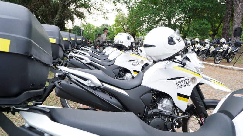 Motocicletas enfileiradas uma ao lado da outra, com o capacete no guidão de cada moto. A foto foi tirada na lateral das motos, possibilitando a captura de mais de 10 motos em uma foto.