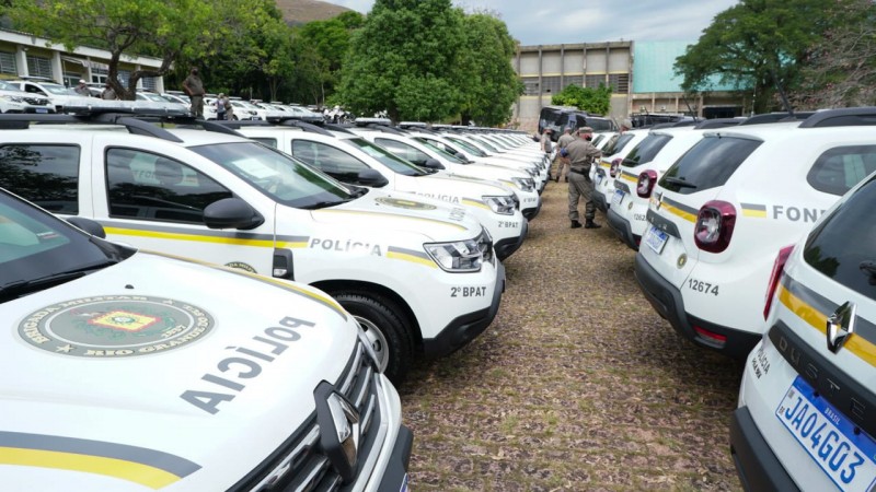 Viaturas estacionadas uma ao lado da outra, são tantas que não é possível contar a quantidade disposta na foto. Alguns policiais militares transitam entre elas.