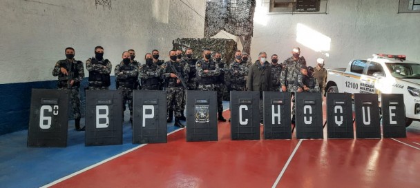 Integrantes do 6º batalhão de choque da Brigada Militar, dentro de galpão esportivo, fardados e de pé. Alguns com as mãos cruzadas e outros com armas. Na sua frente, os escudos pretos utilizados.