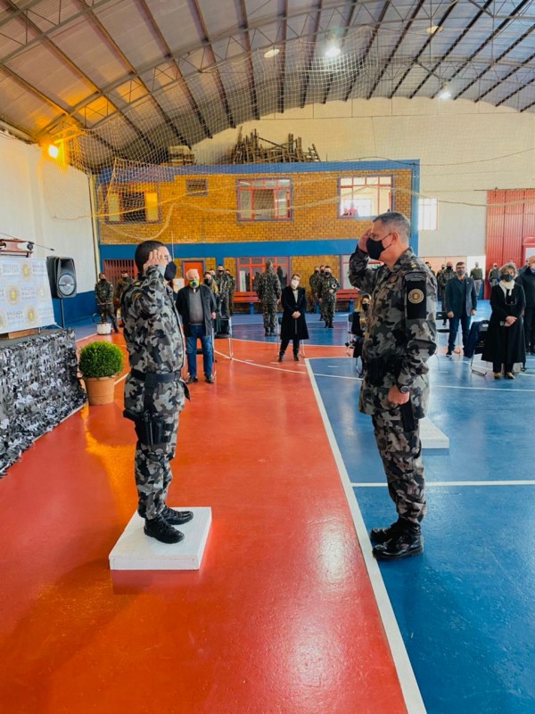 Dois integrantes do 6º BM Chq, um em frente ao outro, prestando continência enquanto outros integrantes assistem.