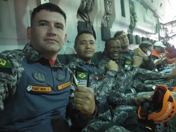 Sargento Picoli aparece ao lado de bombeiros de outros Estados dentro de um avião da FAB. Todos mostram o punho cerrado da mão esquerda.