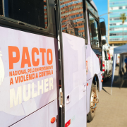 Parte lateral do ônibus lilás com adesivo escrito: Pacto nacional pelo enfrentamento a violência contra a mulher. Ao lado da escrita, logo com símbolo do gênero feminino com mãos dadas.