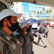 Três integrantes da Brigada Militar, na sombra do toldo do ônibus da Brigada Militar.