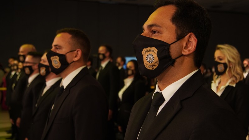 Imagem fechada, mostrando os agentes formandos, com máscara estilizadas com o brasão da Polícia Civil