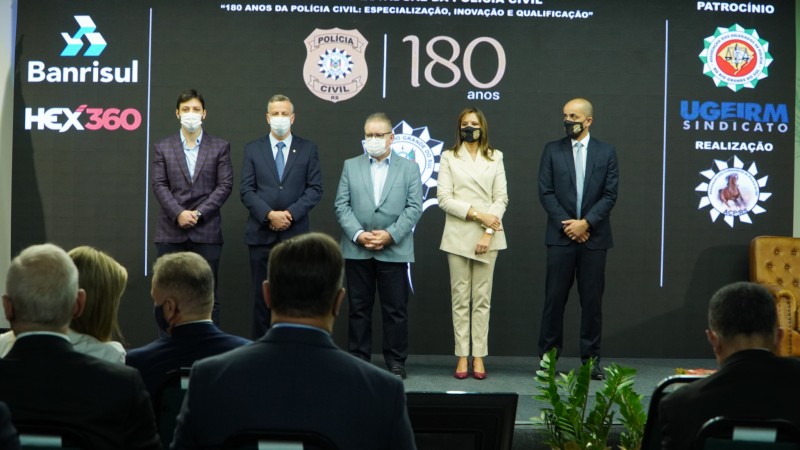 Em frente a um telão com a marca de 180 anos da Polícia Civil e logo dos patrocinadores, em pé, da esquerda para direita: o vice-prefeito de Canela, Gilberto Cezar, o titular da Senad, Luiz Beggiora, o vice-governador, Ranolfo Vieira Júnior, a chefe da PC, Nadine Anflor, e o subchefe, Fábio Motta Lopes.