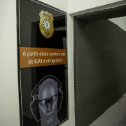 Placa na entrada do estande avisando a obrigatoriedade de E.P.I ao passar da porta.