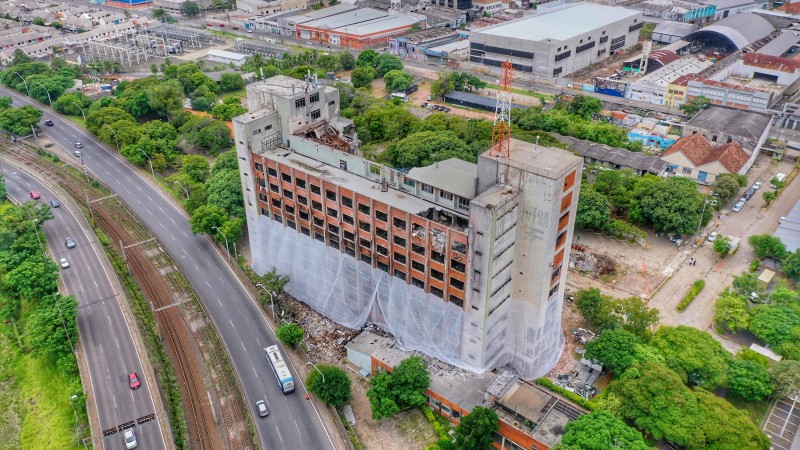 Foto aérea mostra à esquerda trecho a Avenida Castelo Branco e logo ao lado, à direita, face posterior do prédio da SSP, envolto até o quarto andar com telas de proteção. Ao fundo, outros imóveis da região.