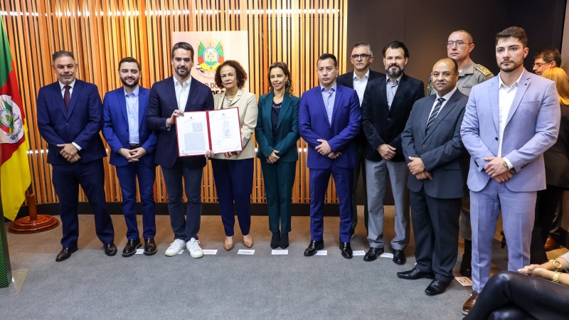 O governador Eduardo Leite, ao lado da presidente do TJ, Iris Helena, segura uma mostrando o termo de cooperação assinado. Ao deles, também posam para foto o vice-governador, Gabriel Souza, o procurador-geral de Justiça, Marcelo Dornelles, os secretários da SSP, Sandro Caron, e da SSPS, Luiz Henrique Viana, o diretor executivo do RS Seguro, Alexandre Padilha, o chefe da PC, Fernando Sodré, o comandante da BM, Cel. Feoli, e o chefe da Susepe, Mateus Schwartz.