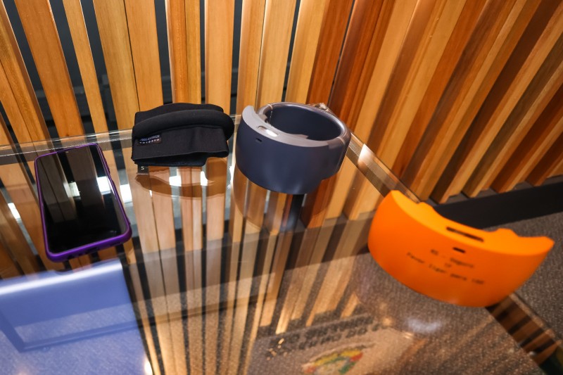 Sobre uma mesa com tampo de vidro, celular e tornozeleira eletrônica que compõem o kit de equipamentos utilizado no projeto de monitoramento de agressores de mulheres.