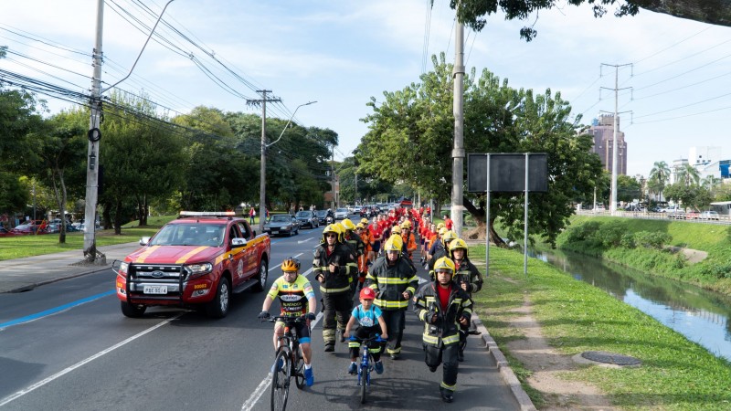 Foto mostra bombeiros equipados correndo em rua ao longo de rio.