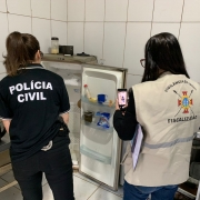 Foto mostra agentes da Polícia Civil e da Vigilância diante de geladeira