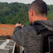 Foto mostra policial de costas com arma em punho sobre telhado de residência