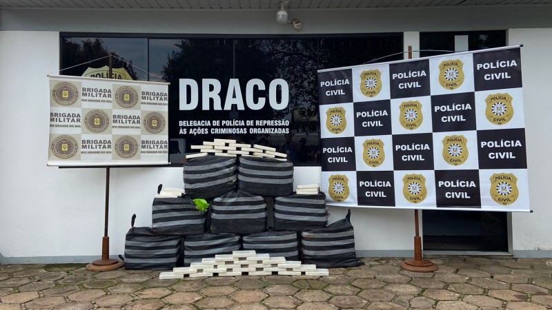 Material apreendido empilhado em frente a banner da BM, da PC e da Draco