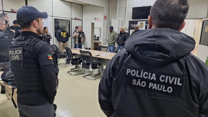 Foto mostra policiais civis ao redor de mesa. Na jaqueta de um dos homens, se lê Polícia Civil São Paulo.