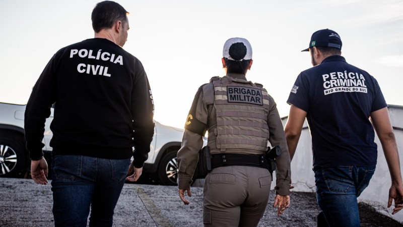 Um policial civil, uma policial militar e um perito criminal, de costas, em movimento, com o céu nublado ao fundo