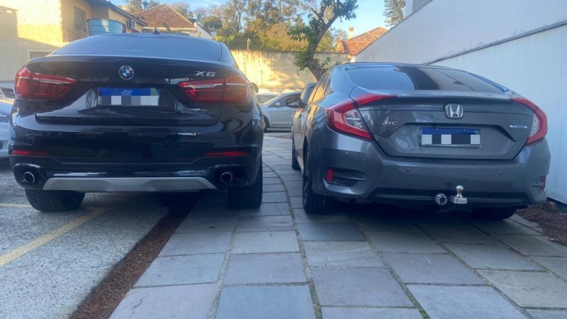 Foto mostra traseira de dois veículos (um Honda e um BMW) estacionados lado a lado em área externa.