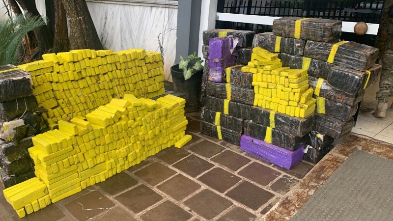 Imagem mostra duas grandes pilhas de tabletes de maconha nas cores amarela, preta e roxa