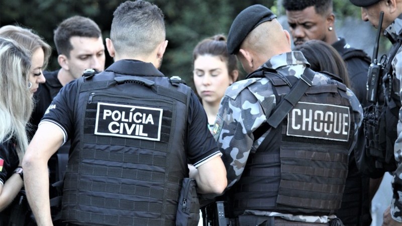 Foto mostra grupo de policiais reunidos em círculo. No colete de um deles, se lê Polícia Civil. No outro, se lê Choque.