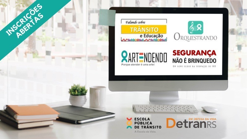 Mesa com alguns cadernos e computador, no qual a tela mostra o logo dos quatro cursos que estão com inscrições abertas
