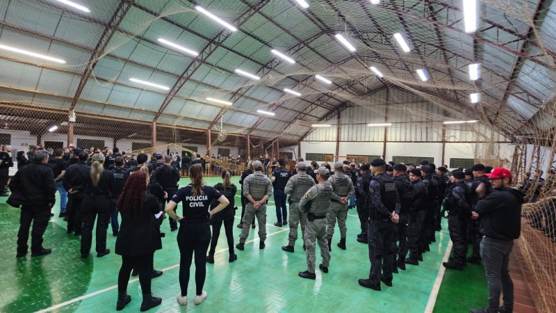 Foto mostra policiais civis e militares em ginásio durante briefing da operação. 