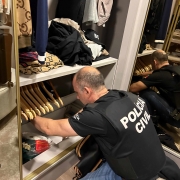 A foto mostra um agente de polícia fazendo buscas no interior de uma residência 