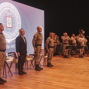 A imagem mostra oficiais e autoridades perfiladas durante execução de uma canção pela banda da Brigada Militar