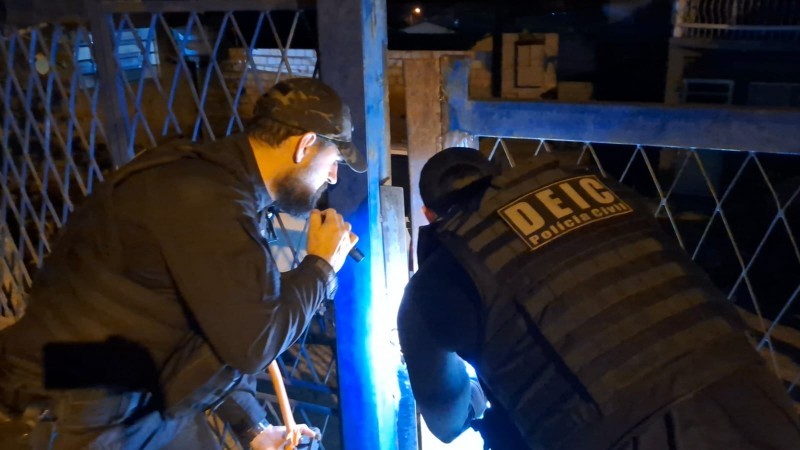 A imagem mostra dois agentes cumprindo mandato de busca e apreensão durante a operação policial