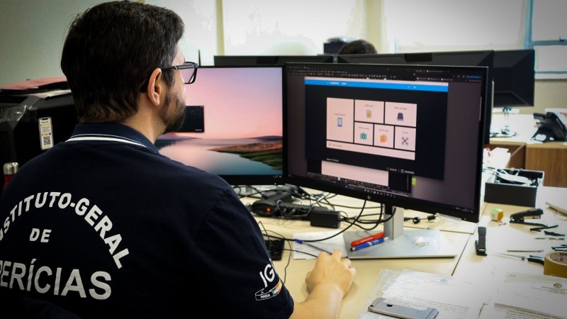 Um homem, com camisa onde se lê nas costas "Instituto-Geral de Perícias", trabalha em um computador.