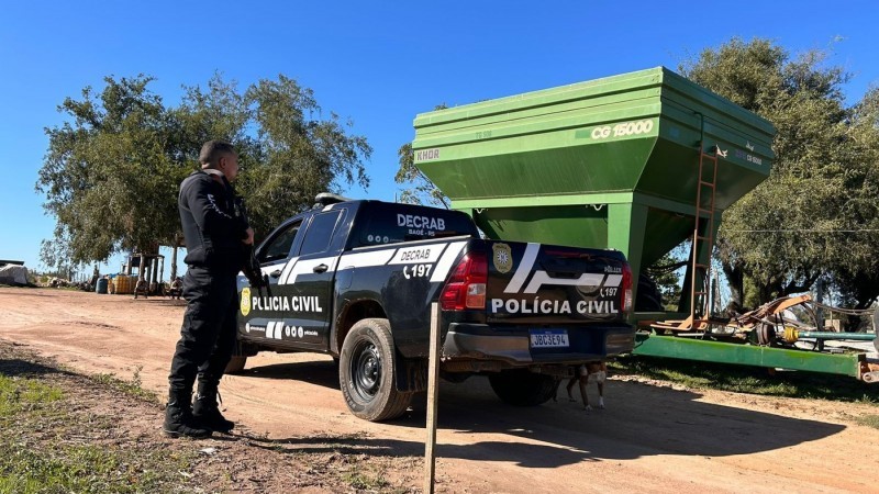 Agente da Polícia Civil em pé, diante da camionete da corporação, em frente ao graneleiro de cor verde apreendido na operação.