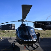 Helicóptero preto da Polícia Civil visto de frente. A aeronave está pousada no local do evento. 