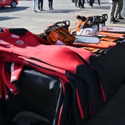 Sobre a mesa, traje vermelho de neoprene com identificação "Bombeiros", luvas e motosserras.