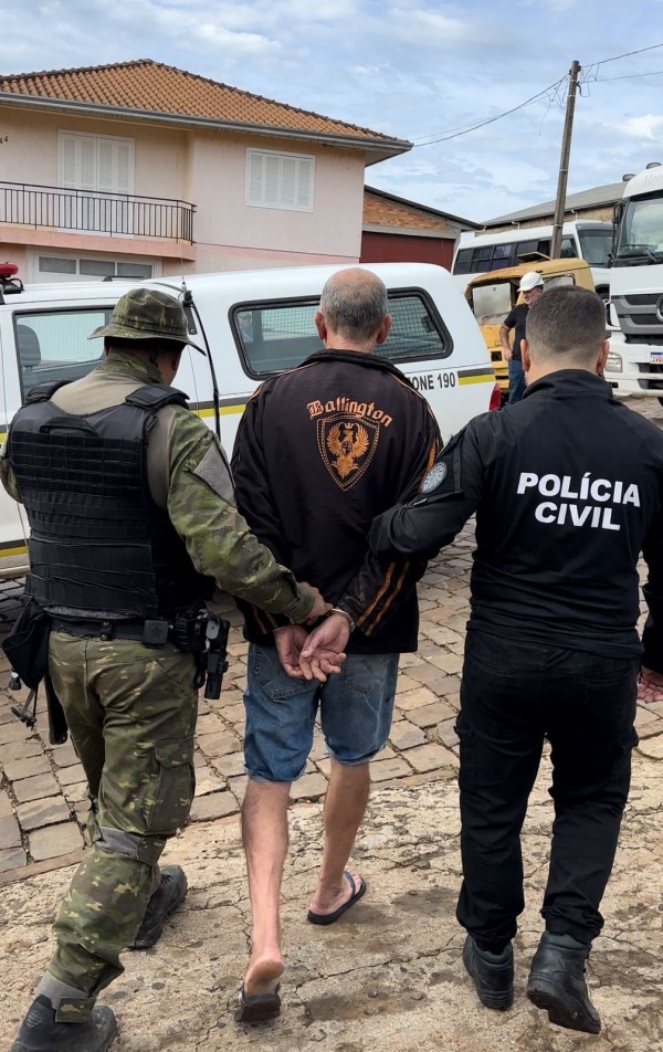 Policiais civis vestidos com coletes a prova de balas conduzem o proprietário do desmanche, preso em flagrante por crime ambiental. 
