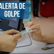 A foto destaca um documento de identidade sendo entregue por um atendente do IGP a alguém que está sentado à sua frente. Aparecem somente os braços das pessoas. No canto superior esquerdo, há um sinal de alerta (triângulo amarelo com ponto de exclamação) em fundo azul transparente ao lado da mensagem em letras brancas "ALERTA DE GOLPE". No canto inferior direito, o brasão do IGP.