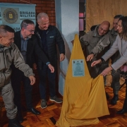 A imagens mostra representantes do comando-geral da Brigada Militar e demais autoridades na cerimônia de inauguração nova base da Corregedoria-Geral. Eles simbolicamente retiram um pano dourado e exibem uma placa que marca a inauguração.