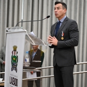 Sandro Caron discursa no púlpito do auditório, já com a medalha afixada no terno.
