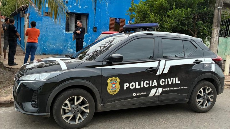 A imagem apresenta em primeiro plano um carro da PC estacionado em frente a uma casa azul, quatro pessoas conversam, sendo dois fardados