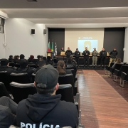 Integrantes da Polícia Civil e da Brigada Militar no auditório do Palácio da Polícia. Seis pessoas estão à frente, uma delas falando para plateia, onde há várias pessoas sentadas com uniformes das corporações.
